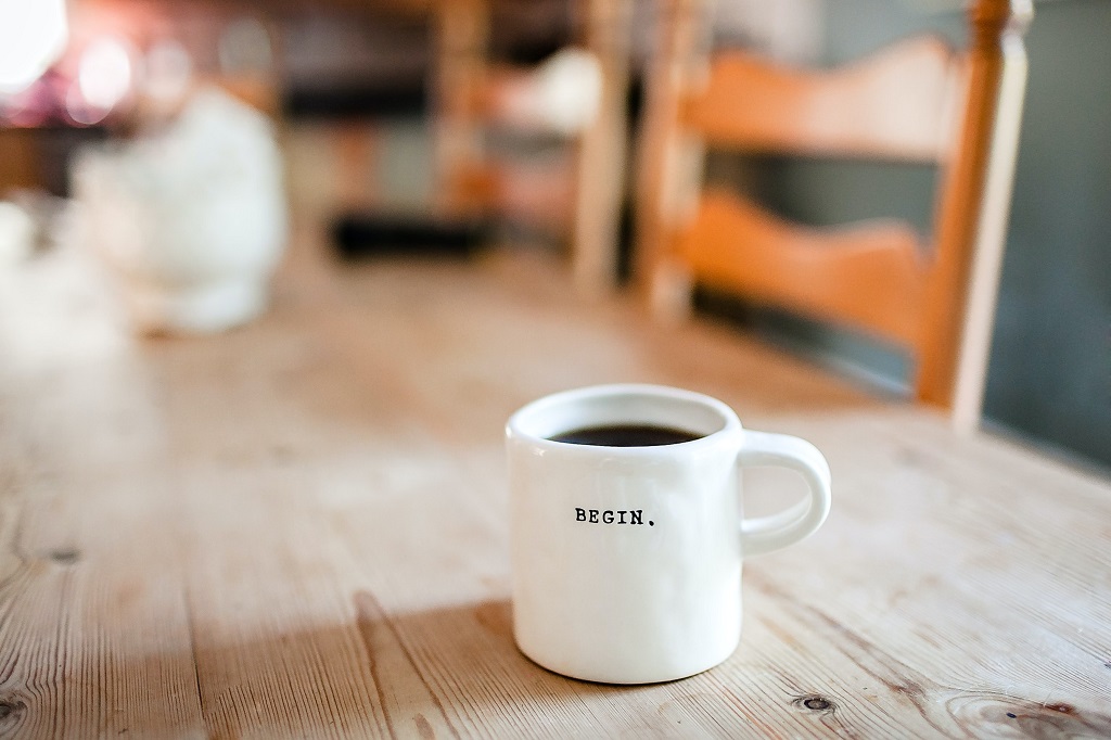 A cup of coffee on the table with notebook and phone placed on it.